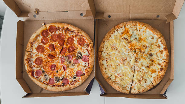 istock Two whole pizzas in open cardboard boxes on white table, one with pepperoni and mushrooms, the other with pineapple and cheese, concept of delivery and fast food, food concept 2224155735