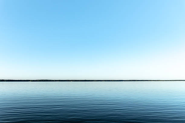Minimalist view of a calm lake under a clear blue sky. Peaceful water surface and clean horizon create a serene and tranquil atmosphere.