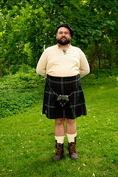 Newlywed portrait outdoors after wedding ceremony. Spouse is a non-binary person, dressed in a Scottish kilt with a beret. Vertical full length outdoors shot. This was taken in Quebec, Canada.