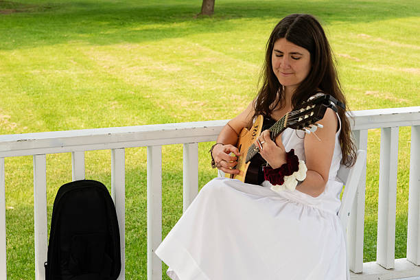 Musician playing for a wedding ceremony outdoors in summer. Woman guitarist is dressed in white. Horizontal full length outdoors shot. This was taken in Quebec, Canada.