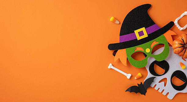 istock Festive Halloween-themed composition featuring decorative masks, candies, pumpkin props, and bone accents on a vibrant orange background 2224158497