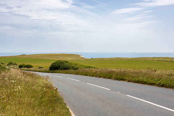 istock An empty, rural asphalt road cutting through bright green fields with sea in the background and bright blue sky above, Isle of Wight, United Kingdom. 2224161629