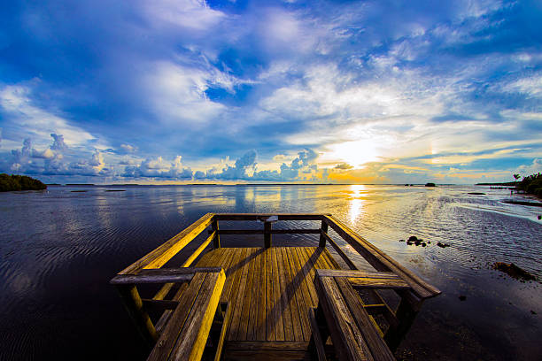 Sunset at the wooden observation deck in the small community of Pineland, Florida.  Pineland is located in Lee County in the southwest part of the state.  Photo taken shortly before sunset on a summer afternoon, scattered clouds against a blue sky.  Note:  photo was taken three years before the devastation of Hurricane Ian struck this area of Florida.