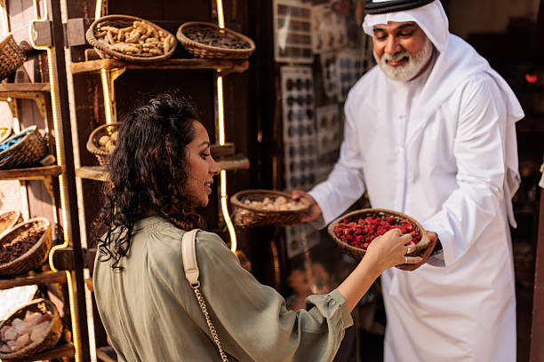 local trader in traditional attire holds a basket of dried spices, engaging with visitors at a colorful and authentic spice shop in Dubai’s heritage market.