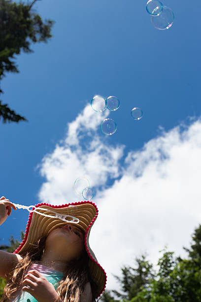 istock Young girl blowing bubbles into a blue sky with clouds 2224186083