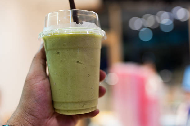 Holding glass of tasty avocado smoothie in a plastic cup