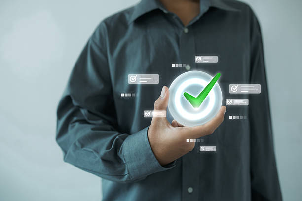 A man in a gray shirt holding a glowing checkmark icon surrounded by task iconsindicating digital approval, completion, or verification in a business context.