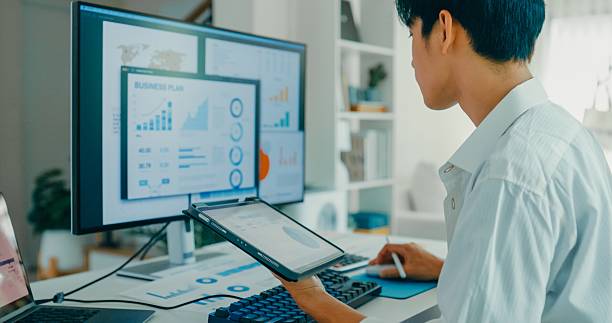 Closeup of young Asian man working from home, using digital tablet for financial data analysis modern remote work environment. Remote work and finance.