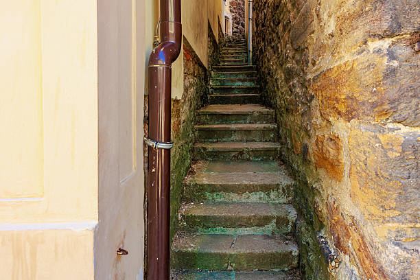 Narrow stone alley with steep steps between historic buildings in bright sunlight.
