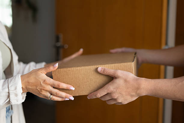 Woman taking cardboard box from male hands, getting logistic package from delivery transportation courier service employee. Deliveryman giving parcel to recipient. Close up of hands