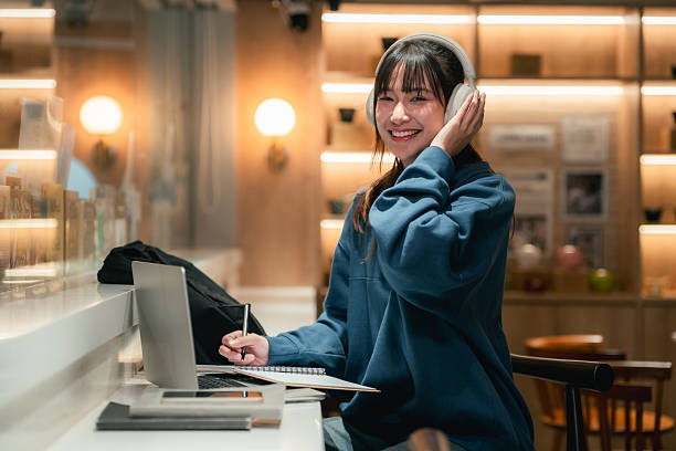 istock Gen Z woman multitasks in a co-working space, listening to an audiobook, taking notes in her book, and studying with her laptop 2224199508
