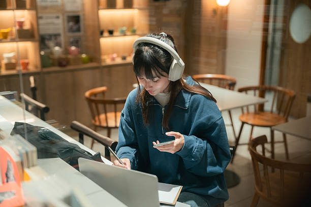 Gen Z woman multitasks in a co-working space, listening to an audiobook, taking notes in her book, and studying with her laptop