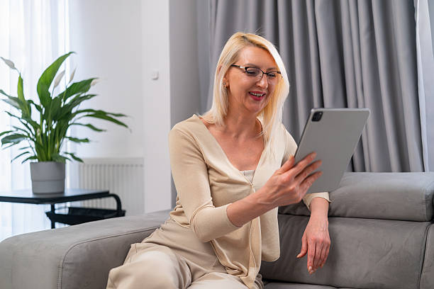 istock Blonde woman chatting with friend online using tablet on couch 2224202589