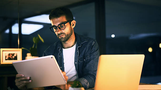 istock Tablet, laptop and man in office at night with creative project with publishing online. Glasses, digital technology and magazine editor with computer for reading article, review deadline or workplace 2224204945