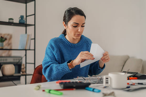 istock Woman opening envelope while calculating domestic bills at home office 2224206322