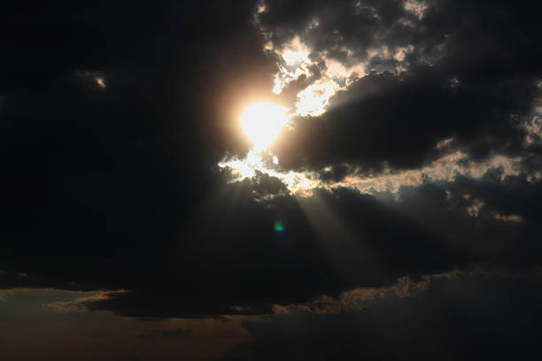 Bright sunlight pierces through dense, dark clouds, creating a stunning contrast in the sky. The scene captures the beauty of late afternoon as rays of light shine down, illuminating the landscape below while the remaining clouds loom above, adding a sense of drama to the atmosphere.