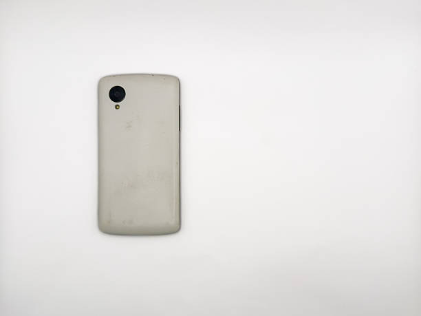 A white cell phone is laying on a white surface. copy space, flay lay, top view. The back of the phone is missing. The phone is not in use