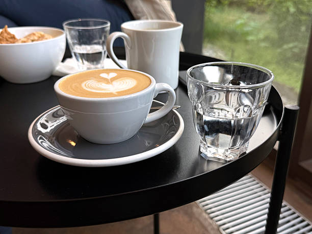 Morning Cafe Scene: Cappuccino and Water on Black Table. Handheld Phone Photo, Selective Focus, Sunlight, Non-AI