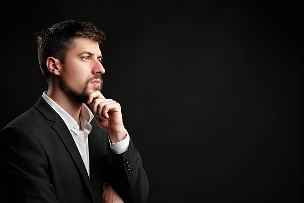 istock Man in a business suit contemplating ideas against a dark background in a studio setting 2224210653