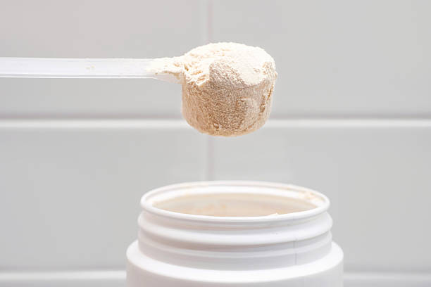 istock Protein powder in scoop from plastic jar side view on gray background close-up. 2224213780