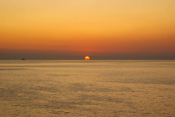 Golden hour casting a warm glow over a tranquil ocean, with a distant ship gracefully sailing along the horizon during sunset