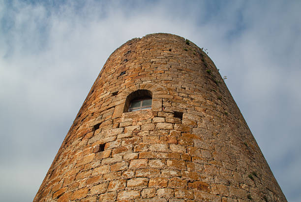 Low angle view of an old stone tower against a cloudy sky, showcasing its weathered texture and small window