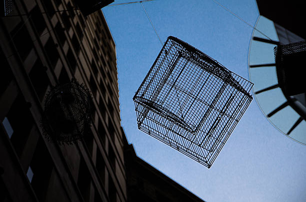A Birdcage hanging over the street against blue sky in dark shadow.