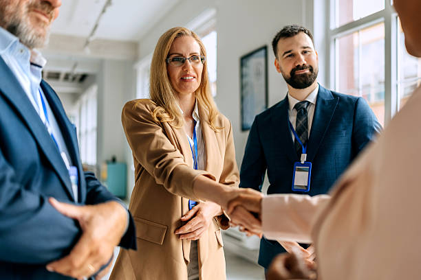 istock Two female colleagues shaking hands while standing with their colleagues at modern office 2224220265