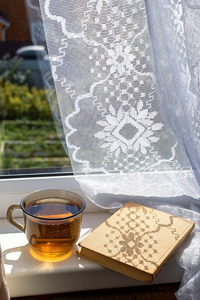 istock Sunlight casts intricate patterns through lace curtains, illuminating a warm cup of tea and book on a windowsill 2224225689