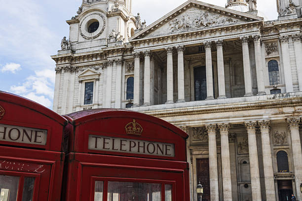 Two classic red phone boxes stand before St Paul Cathedral ornate columns. London, UK, 5 May 2024