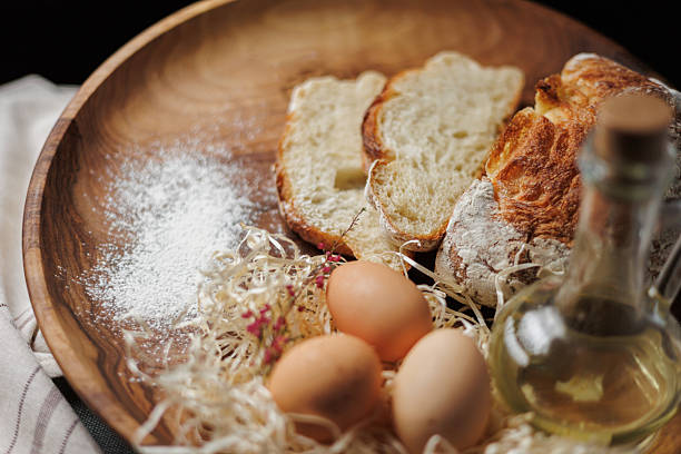 A close-up view of a rustic wooden plate showcasing freshly baked bread, eggs, salt, and oil, emphasizing a natural and cozy culinary presentation with warm tonal hues