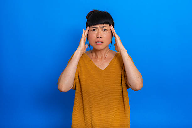 istock Woman experiencing head pain on blue background, looking at camera 2224232294
