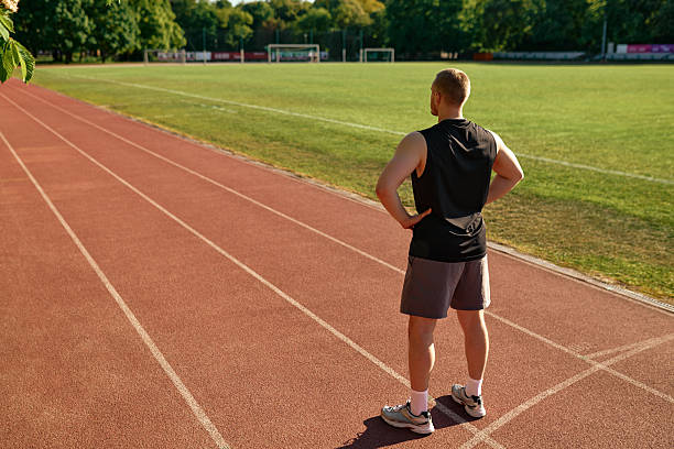 istock Fit man standing on stadium track looking ahead with hands on hips 2224232355