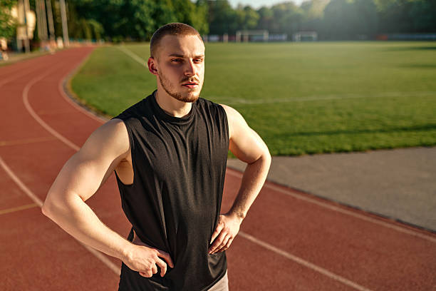Portrait of young muscular man standing on running track with hands on hips after workout. Concept of discipline, strength, and athletic lifestyle.