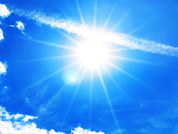A vibrant display of sunlight bursts through a blue sky, creating radiant beams. Wispy clouds add texture to the atmosphere on a beautiful summer day. Space for copy.