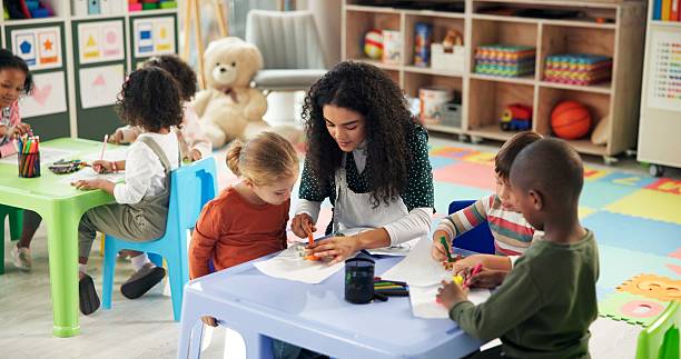 istock Drawing, education and teacher with children in classroom for learning, nursery and creative art. Growth, kindergarten and academy with woman and kids at school for helping and child development 2224235755
