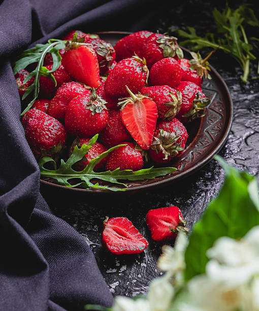 istock Brown plate with fresh strawberries and arugula on a dark background. 2224243324
