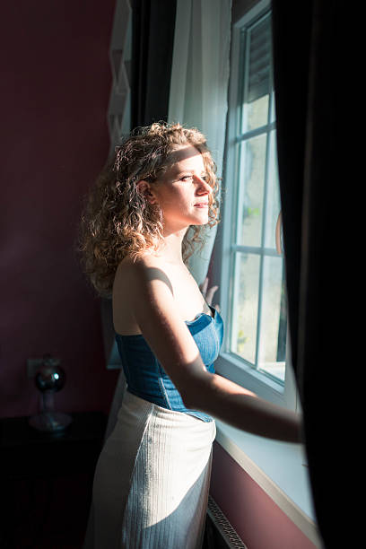 istock Woman Standing by Window Bathed in Sunlight 2224245526