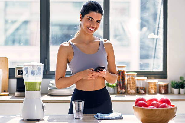 istock Sporty young woman making a vegetable green smoothie while using smartphone in the kitchen at home. 2224254062