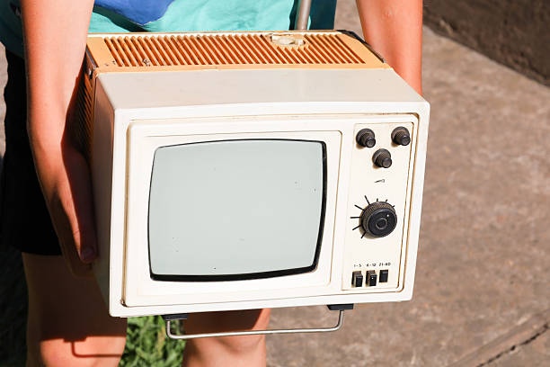 A portable retro television with a black and white screen is held by hands. The classic design of the device with its portable elements evokes nostalgia, highlighting a past era of technology.