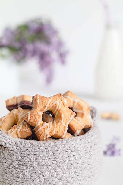 Sun shaped shortbresd cookies in a knitted basket on a blurred background with milk bottle and lilac.