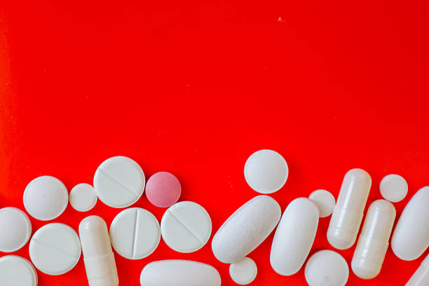istock Various white tablets and one pink, differing in shape and size, are neatly arranged along the right edge of a bright red background. 2224255250