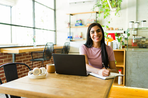 istock Happy woman working remotely in a coffee shop using laptop and notebook 2224255327