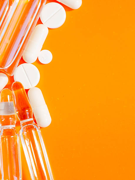istock Bright white tablets, capsules, and clear ampoules are scattered across a vibrant orange background, creating a dynamic composition. 2224255378