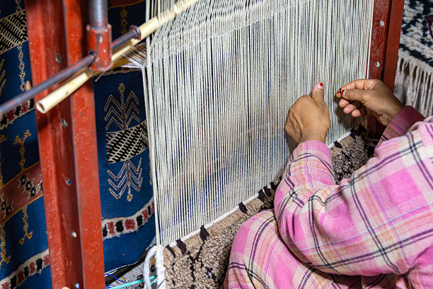 A close-up view of a craftsperson working on a traditional loom, weaving intricate patterns. This image highlights the art of Moroccan weaving craftsmanship with vibrant textiles and delicate handwork.