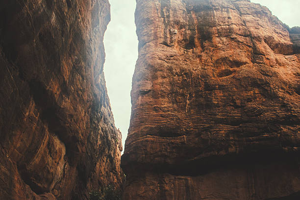 Towering reddish-brown cliffs split by a narrow crevice under a dramatic cloudy sky at Badami, karnataka, India.