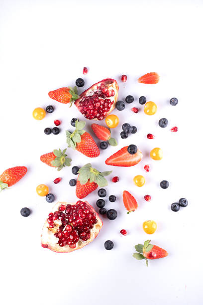 various red fruits strawberry pomegranate blueberry scattered on white background in close up top view