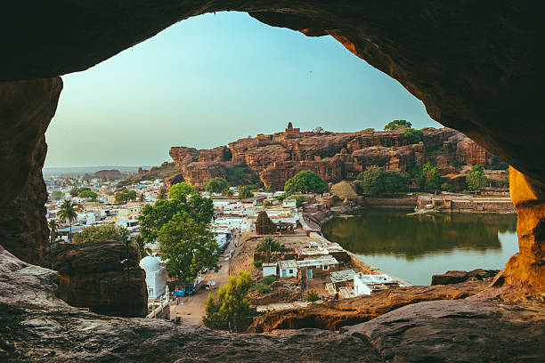 View of Badami town through a cave window, framed by rocky cliffs during golden hour.