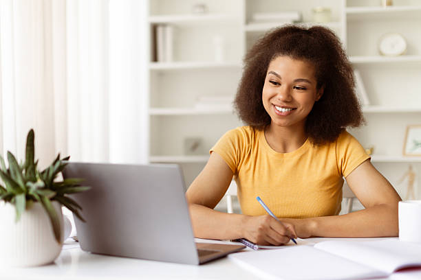 istock Joyful young black woman taking notes while smiling at laptop screen 2224268440