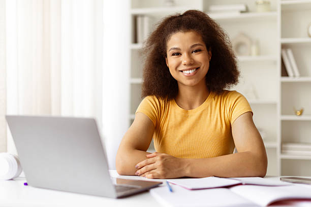 istock Black woman smiling at camera while sitting at home desk with laptop 2224269728